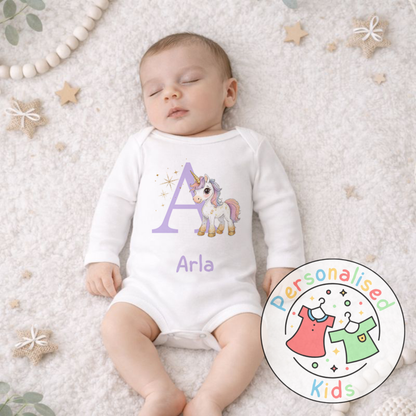 Baby wearing a white onesie with a unicorn design and letter 'A' on a soft surface.