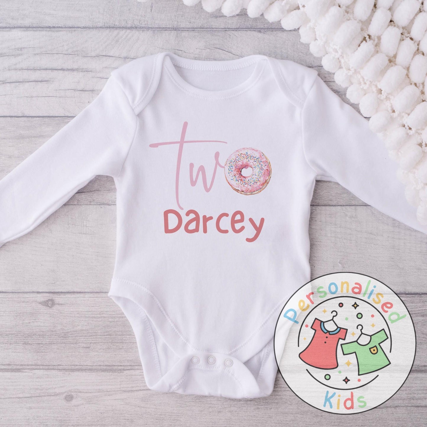 Make their 2nd birthday even sweeter with this adorable personalised donut birthday outfit! Featuring the word “Two” with a sprinkle donut design and your child’s name underneath, this cute top or baby grow is the perfect choice for a birthday celebration, cake smash, or as a special keepsake gift.